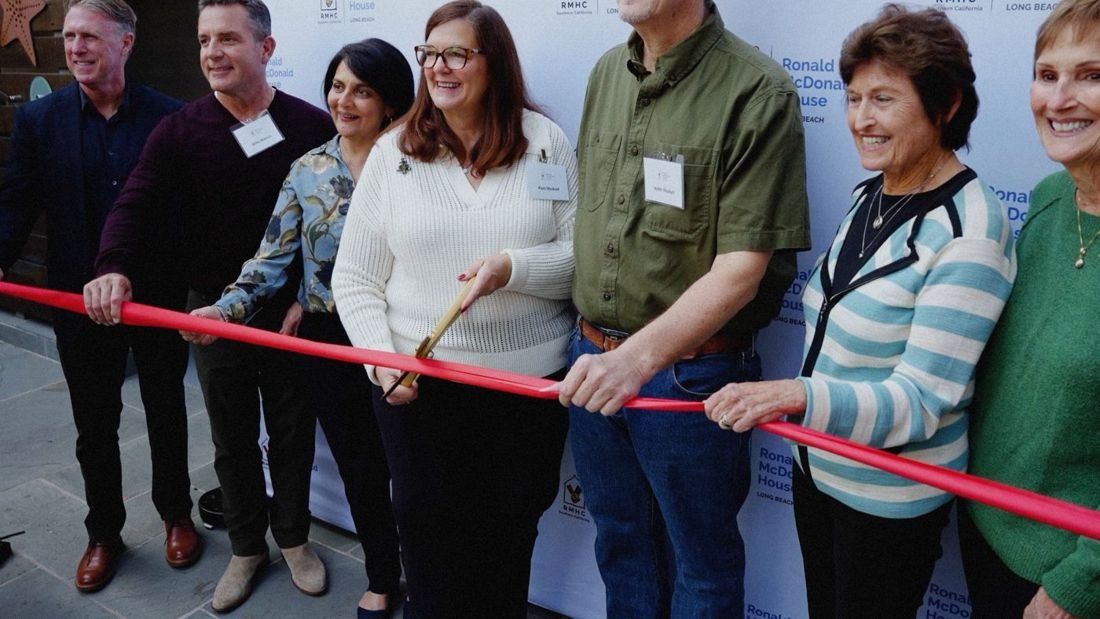 A group cutting a red ribbon at a grand opening